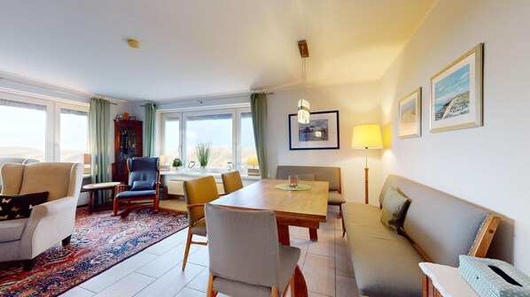 A well-lit living room with a sofa, chairs, a dining table, and a large window.