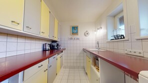 A compact kitchen with yellow and white cabinets, a red countertop, a sink, and a window above the sink.