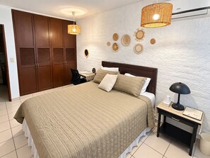 Un dormitorio con una cama grande, un escritorio, una silla, una mesita de noche y un armario.