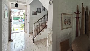 Un escalier avec un mur blanc et une décoration en forme d’attrape-rêves. Il y a une porte qui donne sur l’extérieur et une fenêtre avec vue sur un immeuble.