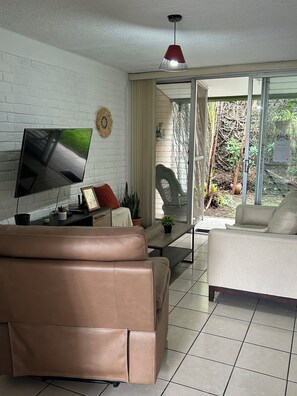 Un salón con televisión de pantalla plana, un sofá marrón, un sofá blanco, una mesa de centro y una lámpara colgante roja.