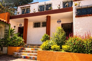 A building with a white facade, colorful tiled steps, and a garden with various plants and flowers.