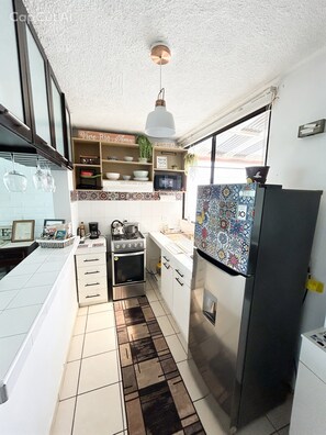 Una cocina compacta con armarios blancos, un refrigerador de acero inoxidable, un microondas y una estufa a gas.