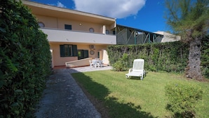 Un edificio de dos pisos con un sendero pavimentado que conduce a una zona verde con mobiliario exterior.