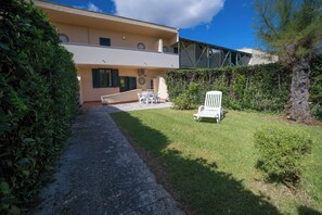 A two-story building with a paved pathway leading to a grassy area with outdoor furniture.