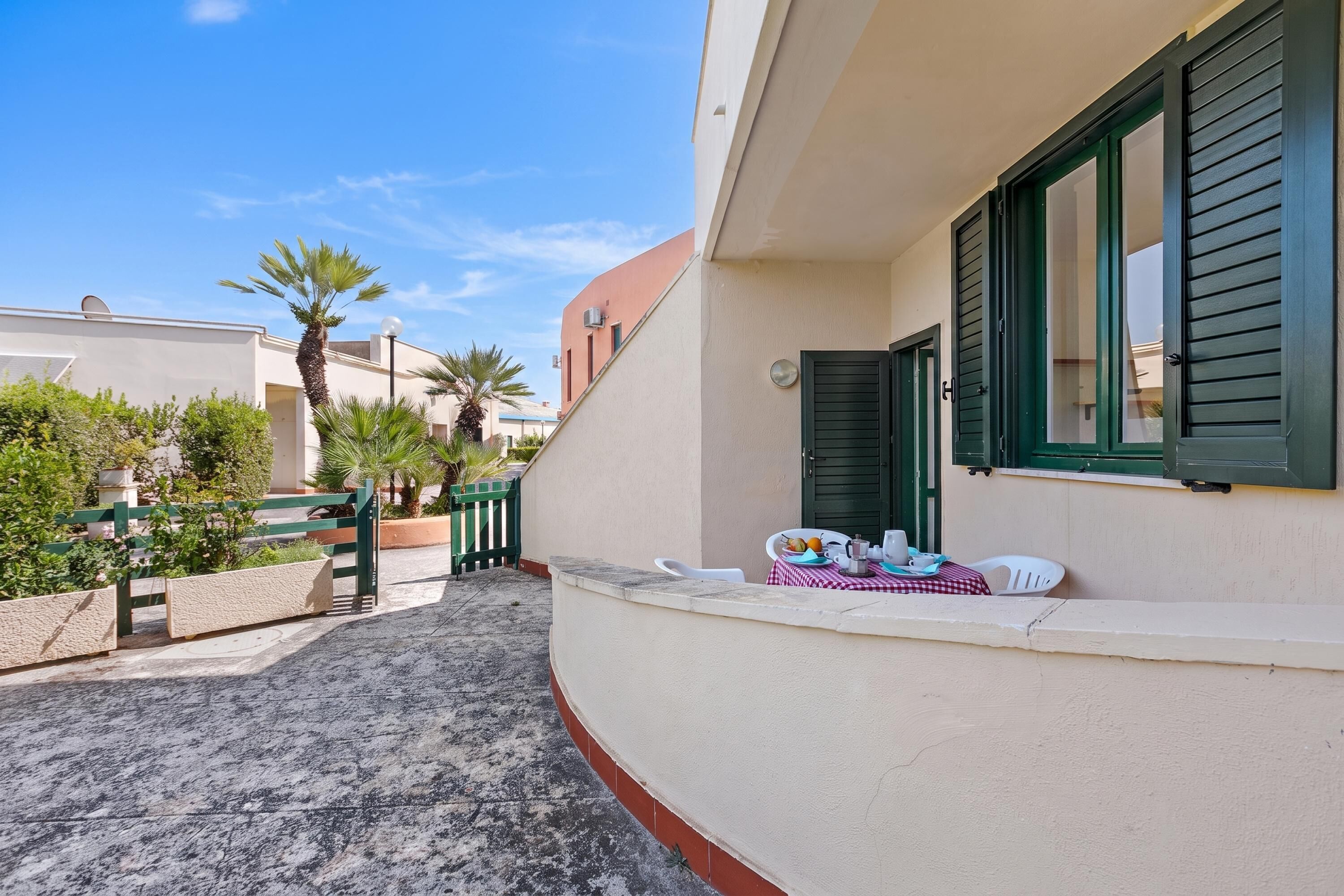 A balcony with a table set for two, a green gate, and a palm tree in the background.