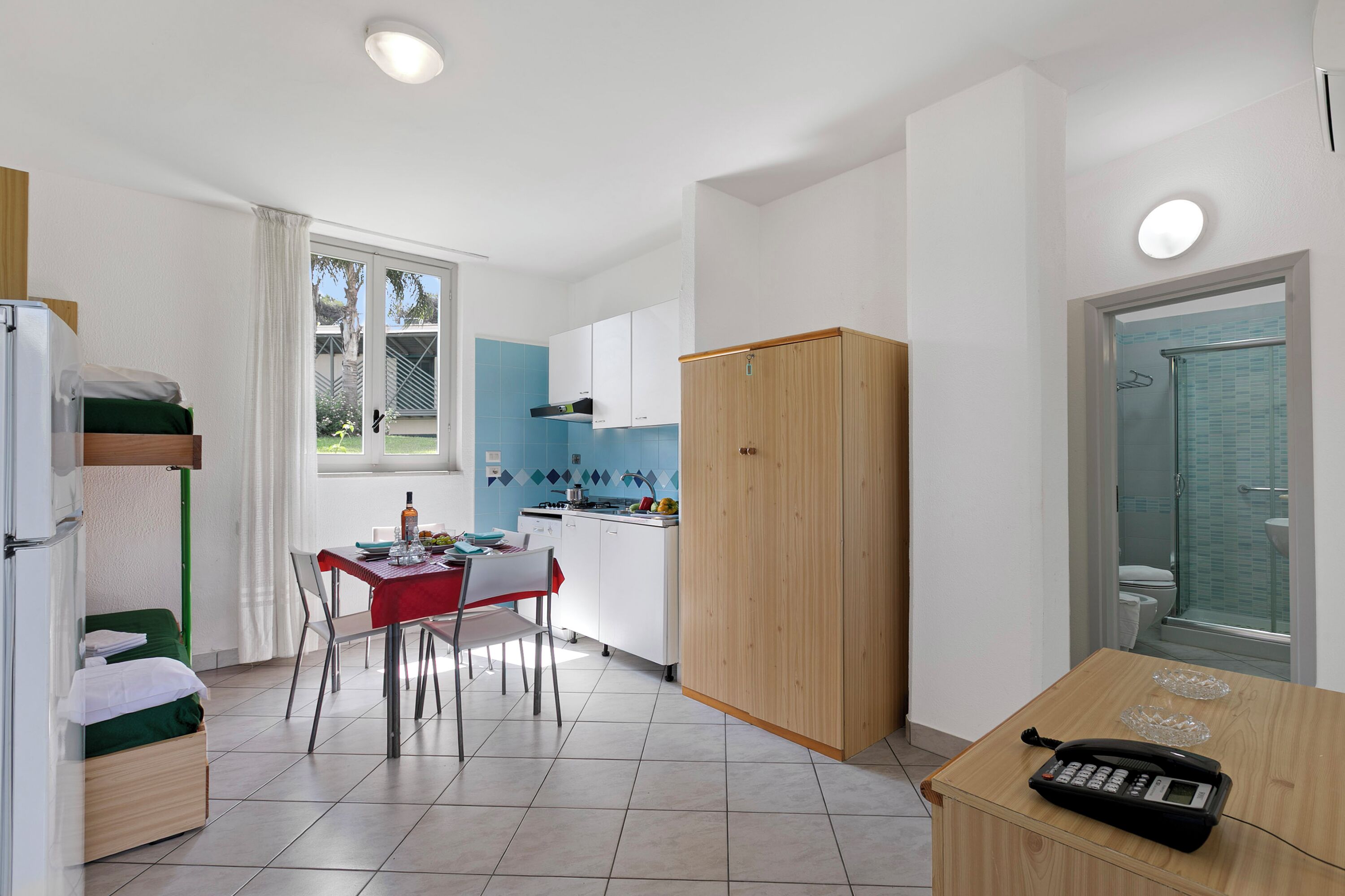 A compact kitchen with a dining area, a small table with a phone, and a view of the outside.