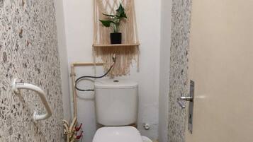 A small bathroom with a macramé shelf holding a potted plant, a toilet, and a checkered floor.