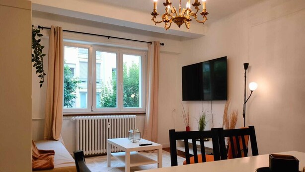 Une pièce confortable avec un lit, une table blanche, un téléviseur et une fenêtre avec des rideaux.