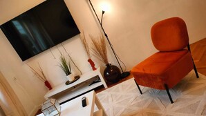 Un salon moderne avec un téléviseur à écran plat fixé au mur, une table basse blanche, un fauteuil orange et un tapis à motifs.