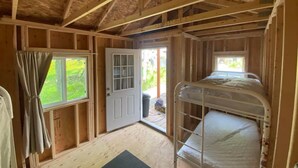 Een kamer met houten wanden en plafond, een stapelbed, een deur naar buiten en een raam met gordijnen.