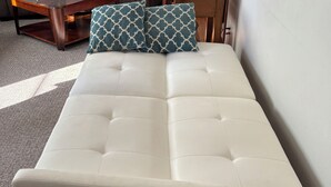 Un canapé blanc à motifs capitonnés, placé sur un plancher en bois avec un tapis.