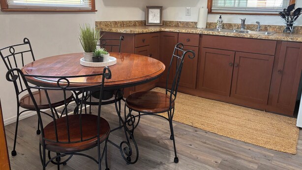 Una cocina con una mesa redonda de madera, cuatro sillas, encimeras de granito, armarios de madera y una ventana con persianas.