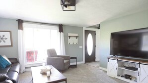 A living room with a sofa, armchair, coffee table, TV, and a sliding door leading to a balcony. - Quiet & charming 3-bedroom, 3-story house located in Butler, Ohio. (Butler)