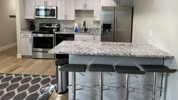 Une cuisine moderne avec des meubles en bois clair, des appareils en acier inoxydable, un plan de travail en marbre et un coin bar avec des tabourets.