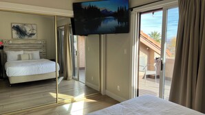 Une chambre d’hôtel avec un lit, une télévision, une porte-fenêtre coulissante donnant sur un balcon et un tableau au mur.