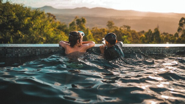 A couple relaxing in a hot tub with a scenic view of mountains and trees.