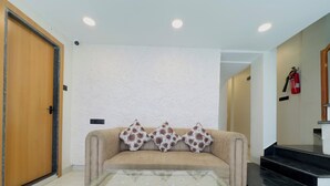 A modern living room with a beige sofa, a glass coffee table, and a patterned throw pillow. - Hotel Sharda Inn (Ujjain)