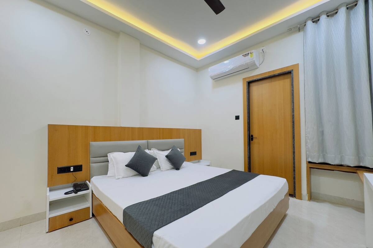 A modern hotel room with a large bed, bedside tables, a wardrobe, and an air conditioning unit.