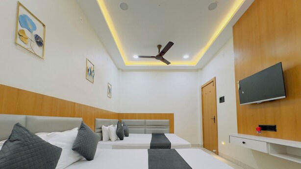 A hotel room with two beds, a ceiling fan, recessed lighting, a TV, and artwork on the walls. - Hotel Sharda Inn (Ujjain)