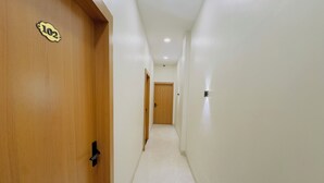 A hallway with a wooden door labeled "102" and a white tiled floor. - Hotel Sharda Inn (Ujjain)