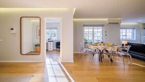 A spacious living area with a dining table, clear chairs, a black sofa, and a large mirror. - Maestro Park Residence (Cascais)