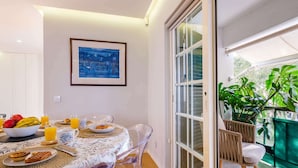 A dining area with a table set for breakfast, a framed artwork on the wall, and a view of greenery outside. - Maestro Park Residence (Cascais)
