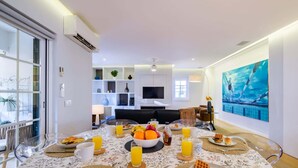 A dining area with a table set for breakfast, a TV in the background, and a large painting on the wall. - Maestro Park Residence (Cascais)