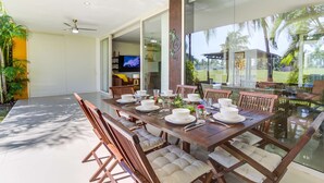 A dining area with a glass table, wooden chairs, and a view of the outdoors.