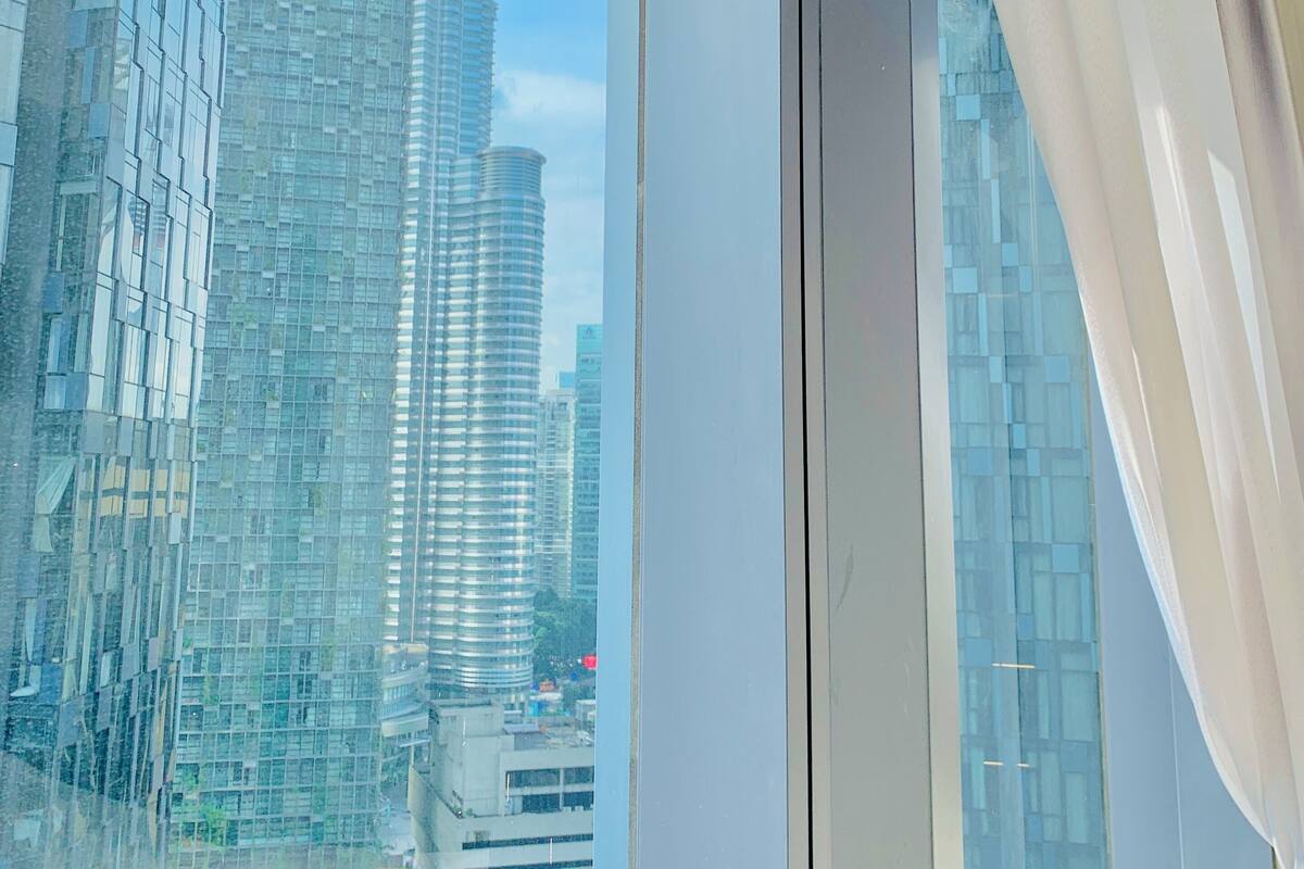 A view through a window with a curtain, featuring modern high-rise buildings and a clear sky.