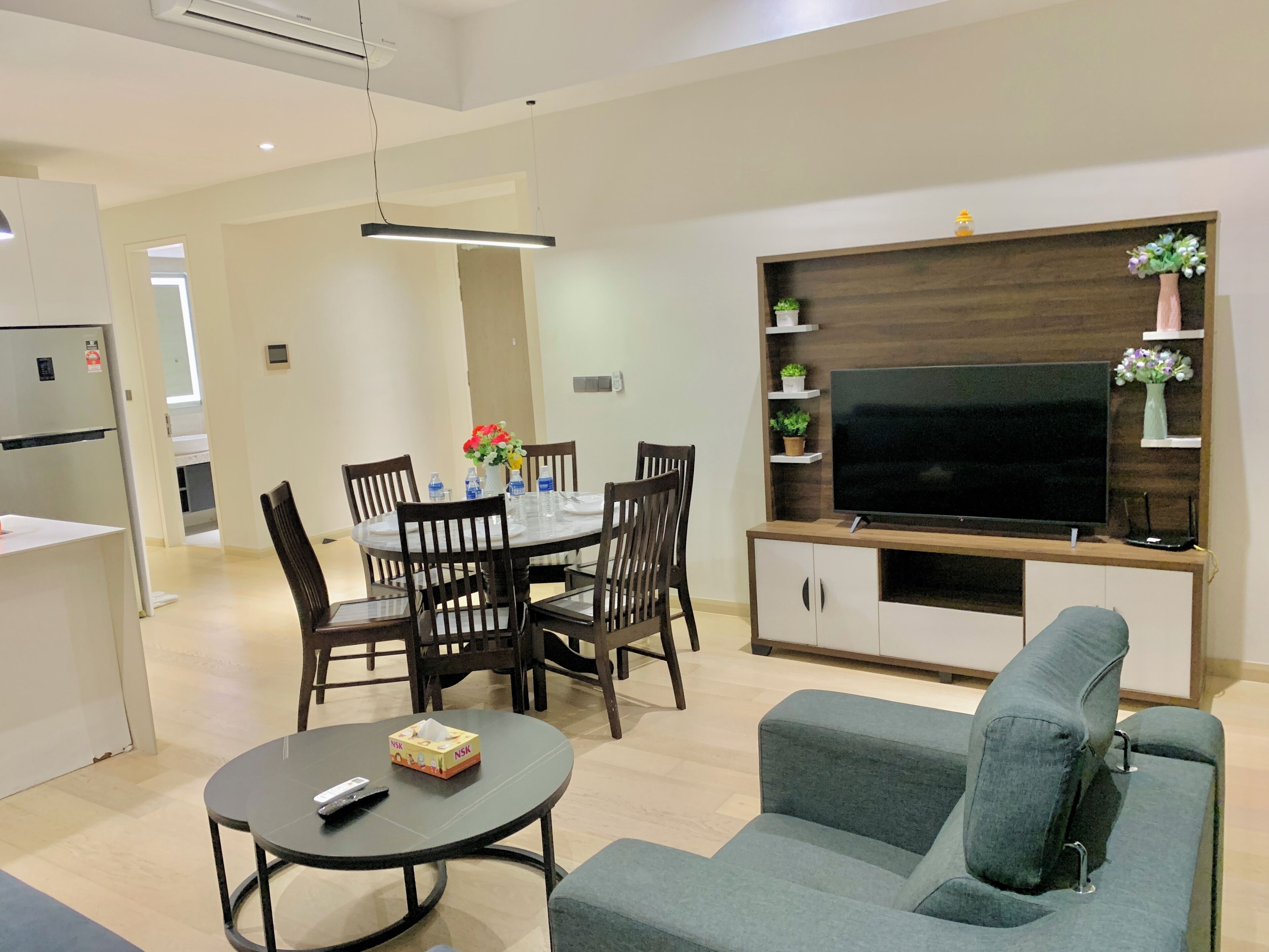 Una sala de estar moderna con sofá, televisión, mesa de comedor con sillas y una cocina al fondo.