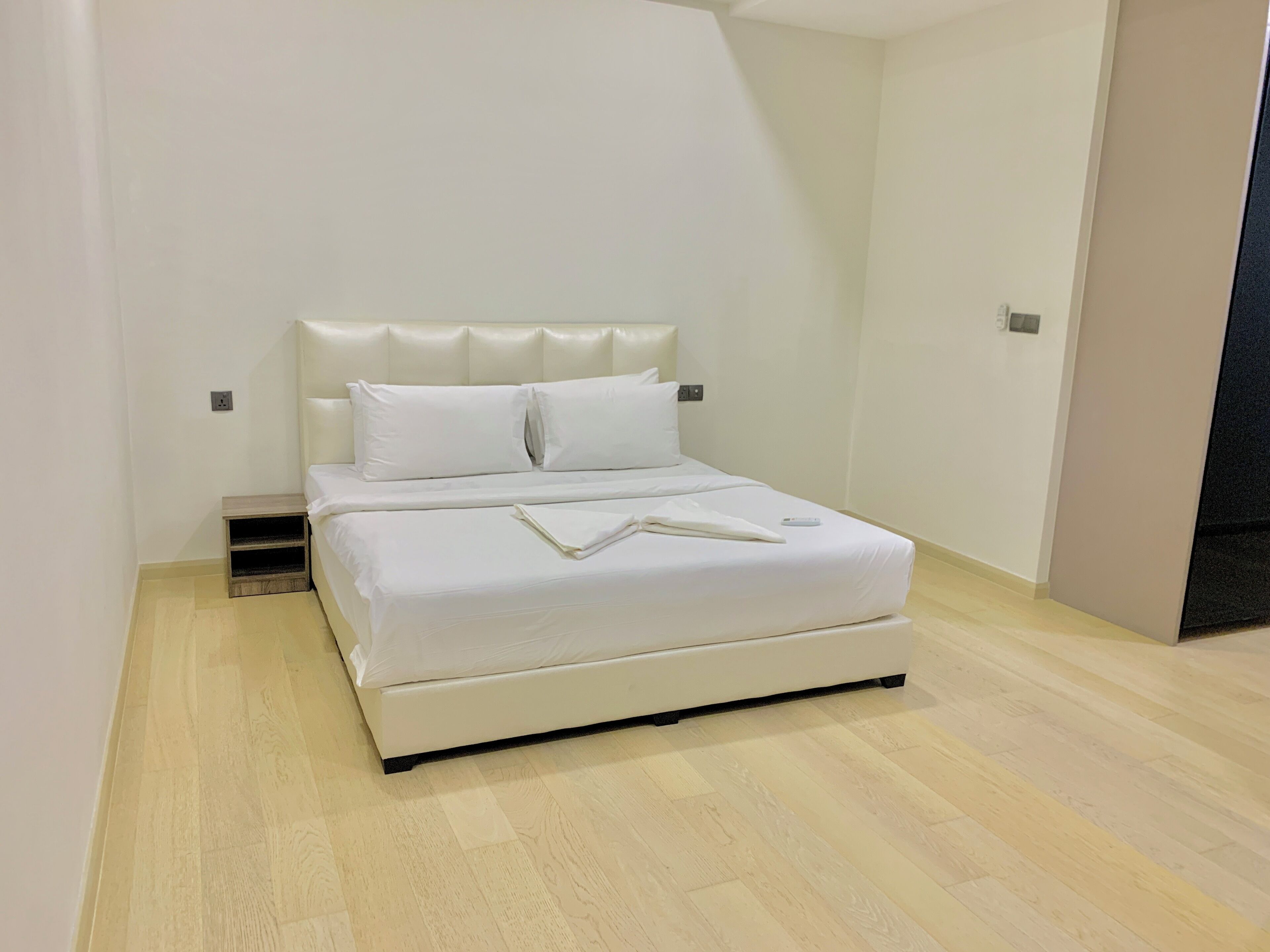Ein modernes Schlafzimmer mit einem weißen Bett, einem Holfnachtkästchen und einem hellen Holzboden.