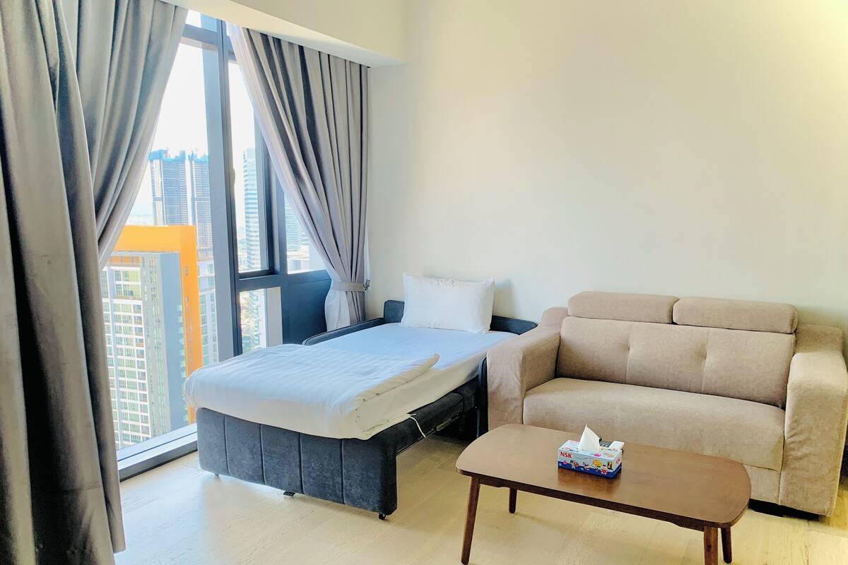 A hotel room with a bed, a sofa, a small table, and a window with curtains.