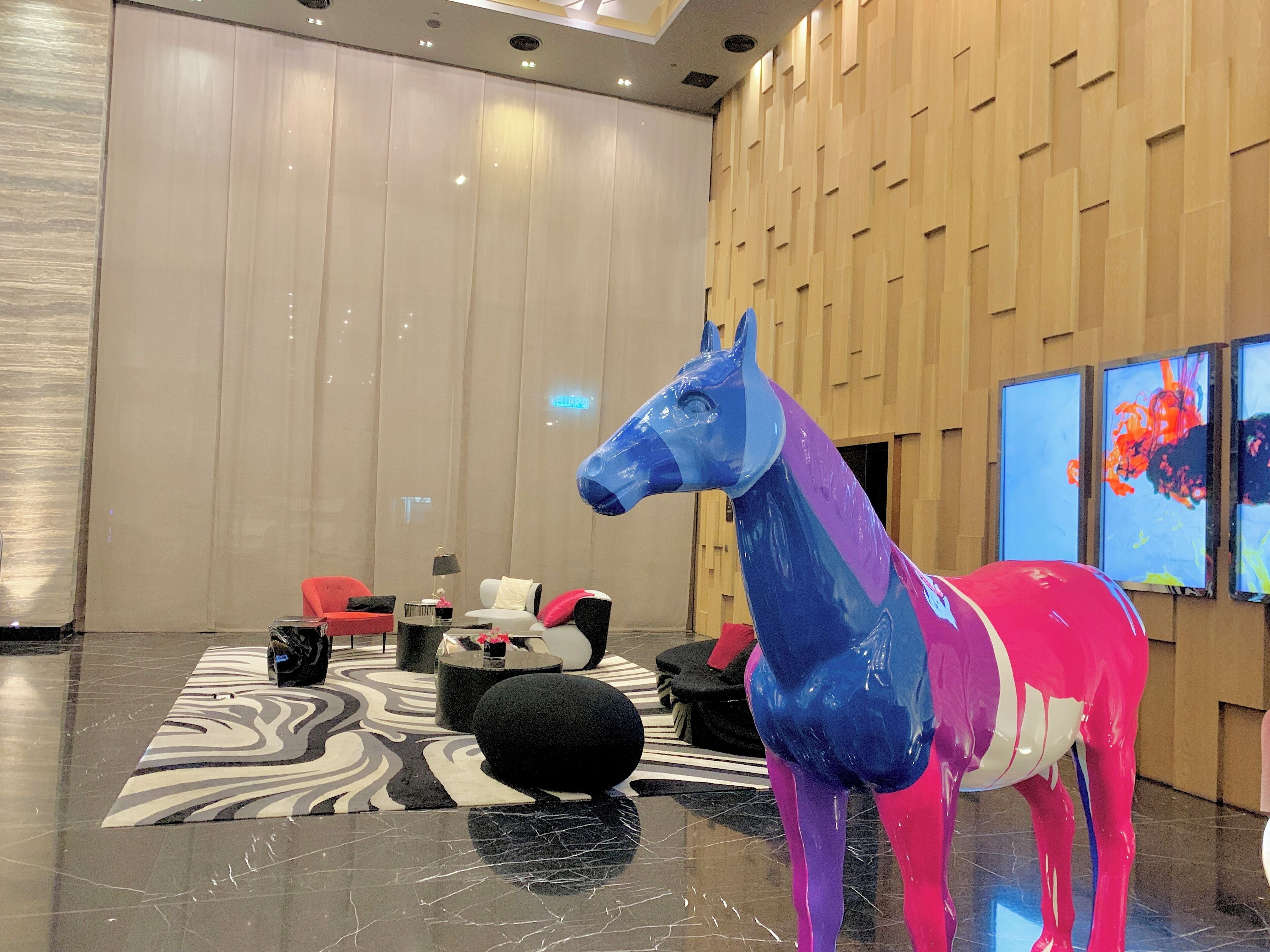 Un vestíbulo moderno con una gran escultura de un caballo azul y rosa, un felpudo con estampado de cebra y una pared de madera con arte abstracto.