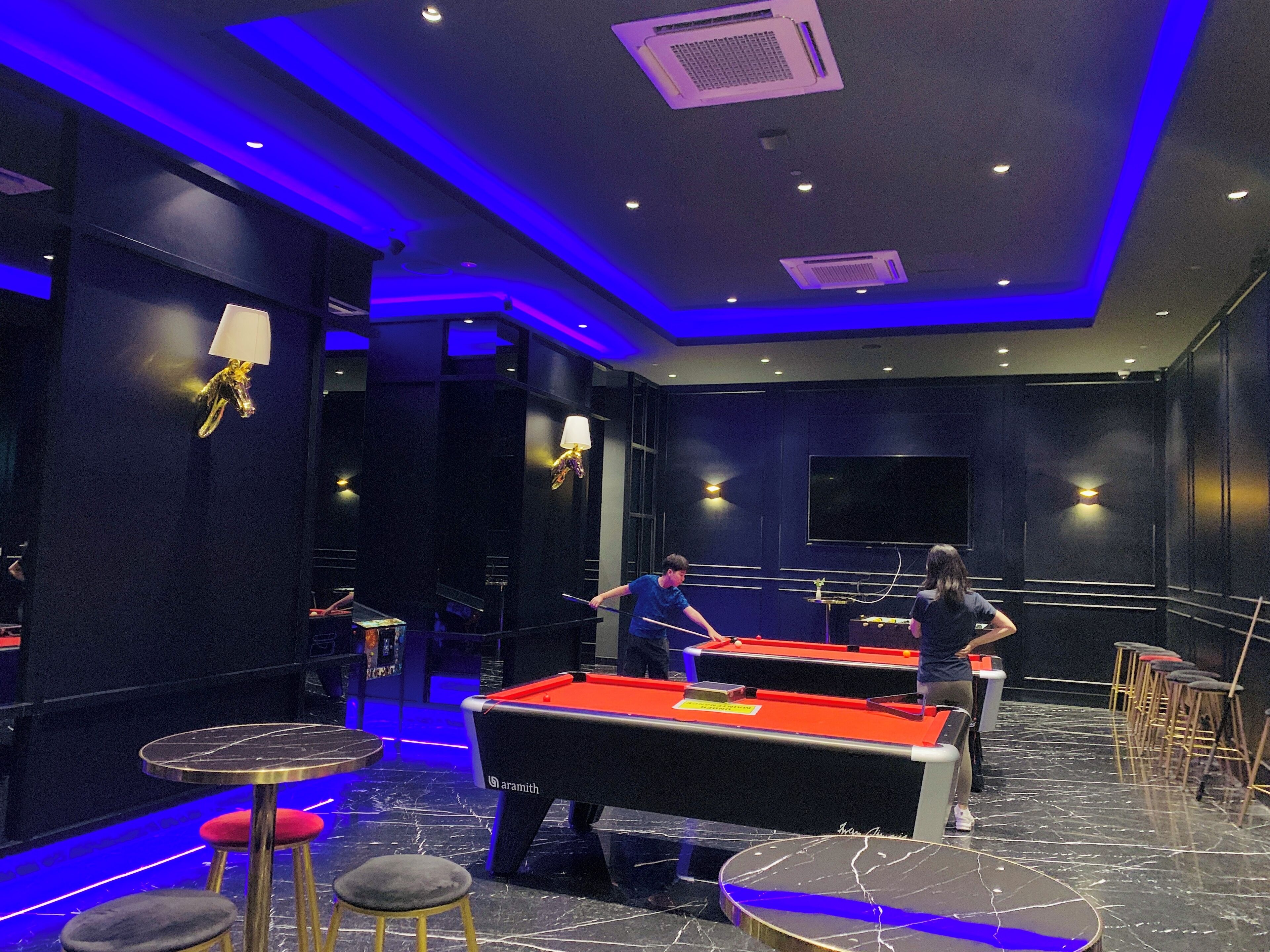 A billiards room with a pool table, stools, and a staircase.