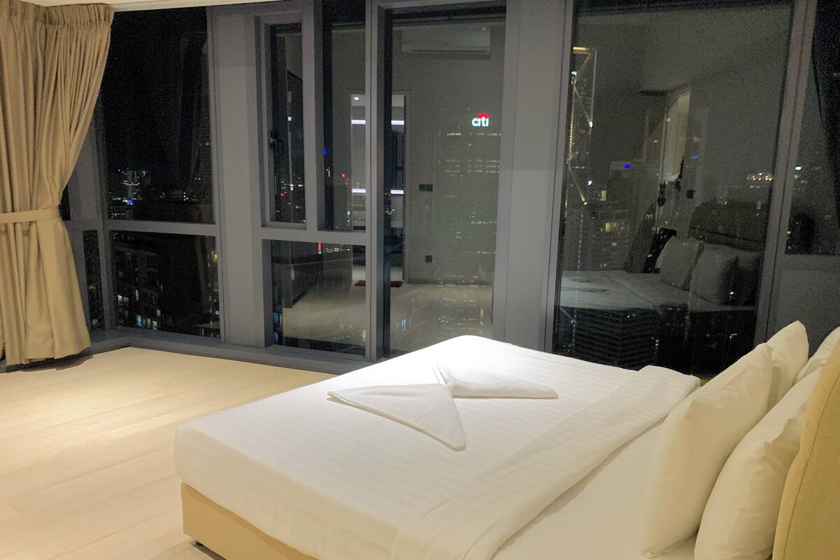 A modern bedroom with a large bed, a view of the cityscape through floor-to-ceiling windows, and a curtain on the left side.