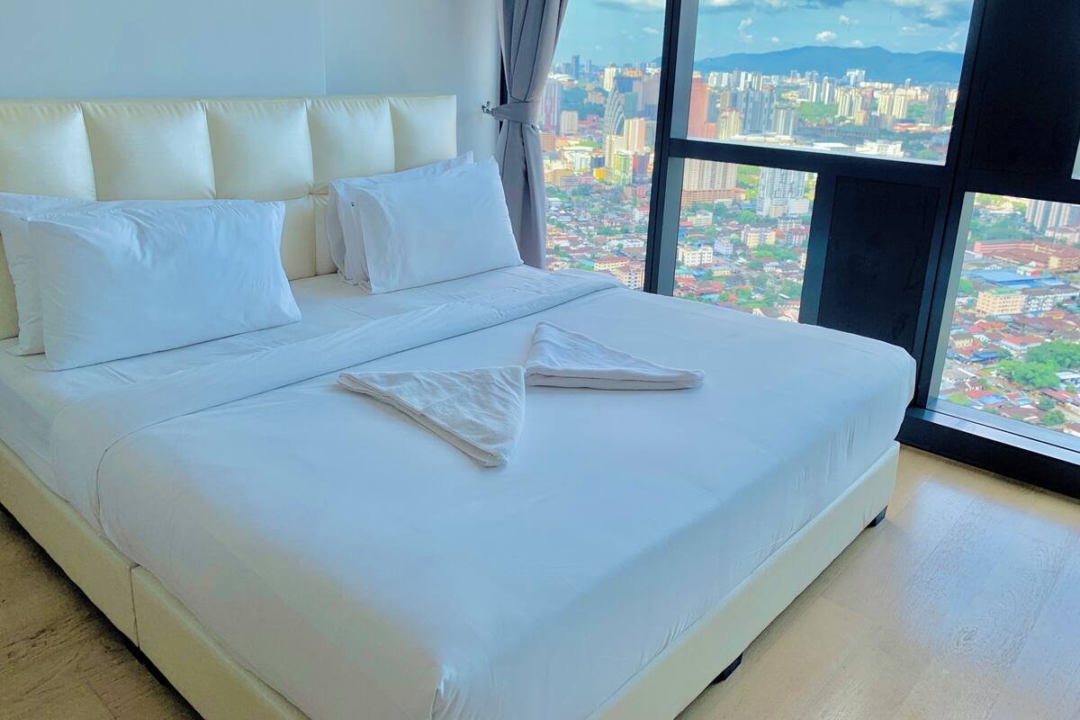 A large bed with white linens in a room with a city view.