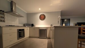 A modern kitchen with white cabinetry, stainless steel appliances, and a central island. - Warm, Cosy winter getaway with Hot Chocolate and Coffee and Heating every room! (Vasse)