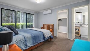 A bedroom with a bed, a nightstand, a lamp, a window with a view of trees, and a bathroom with a mirror and sink. - Warm, Cosy winter getaway with Hot Chocolate and Coffee and Heating every room! (Vasse)