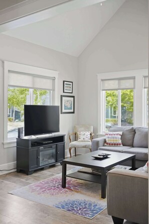 Un salon avec un téléviseur à écran plat posé sur un meuble, un canapé, une table basse et un tapis à motifs.