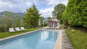 A swimming pool with lounge chairs and a covered seating area, surrounded by greenery and mountains in the background. - La Casetta sul Lago by Interhome (Iseo)