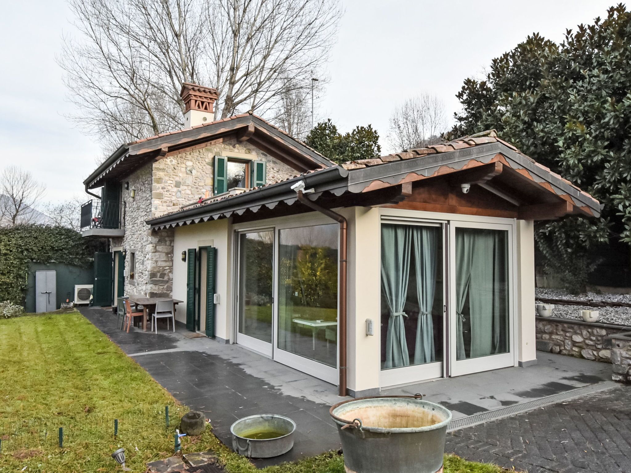 A stone house with a tiled roof, a covered patio, and a large sliding glass door.