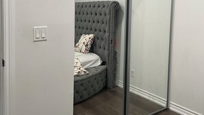 Ein Zimmer mit Schiebeglasdoor, einem grauen Sofa mit Wirbelstickerei, einer weißen Wanduhr und einem Lichtschalter.