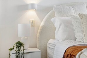 Een verzorgde slaapkamer met een bed, een nachtkastje, een lamp en een wandlamp.