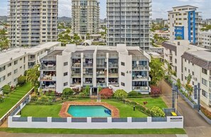 Een meerlaags appartementencomplex met balkons, een zwembad en een verzorgde tuin.