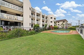 Een appartementencomplex met meerdere balkons, een zwembad en een verzorgd gazon.