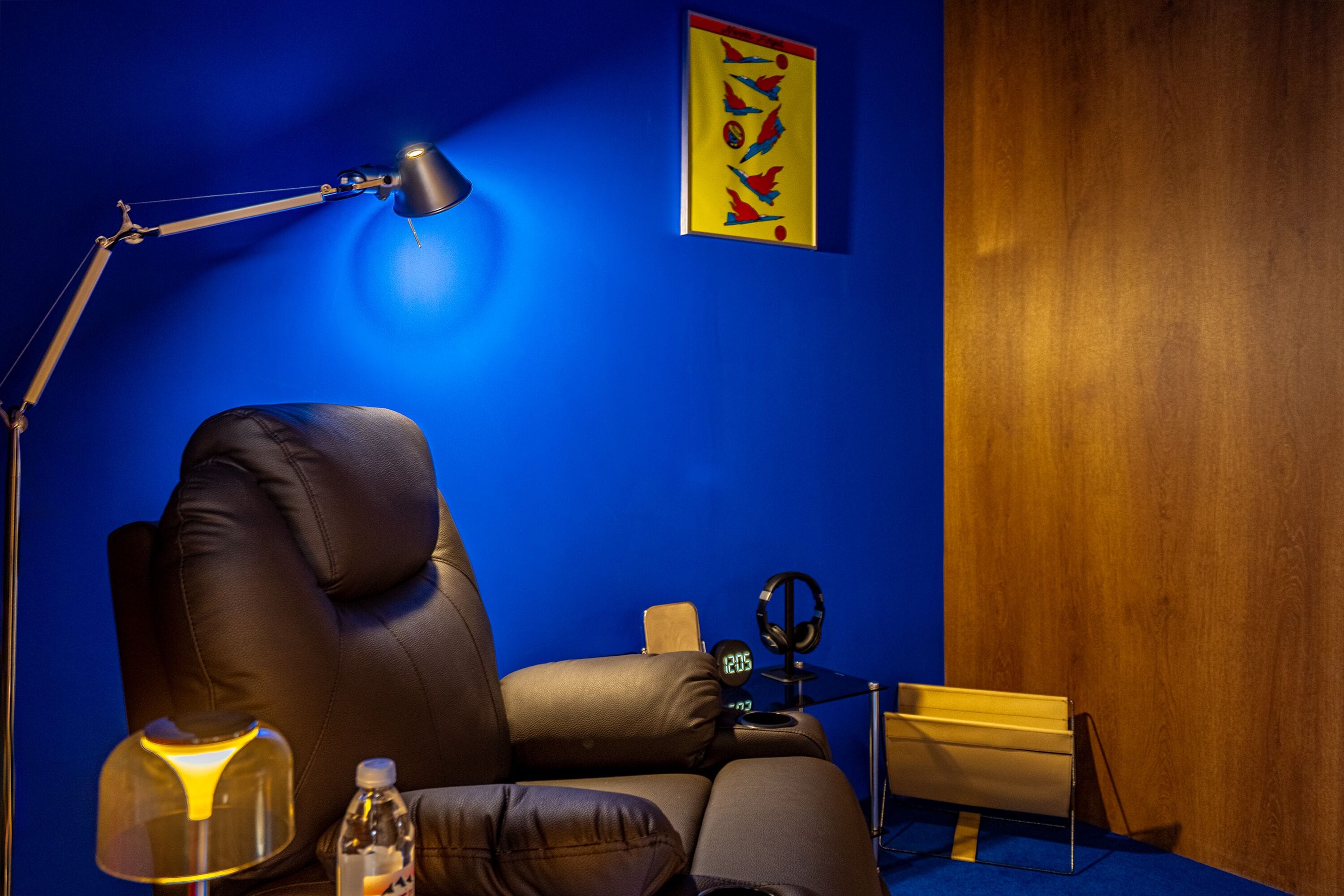 Une pièce avec un mur bleu, un fauteuil en cuir, un bureau avec une lampe, une horloge et un tableau encadré.