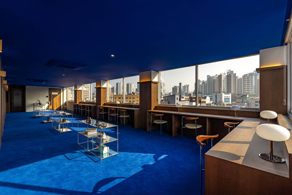 A modern hotel room with a city view, a blue carpet, and a bar area.