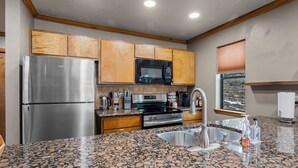 A modern kitchen with granite countertops, stainless steel appliances, wooden cabinets, and a window with blinds. - Updated Angel Fire Golf Lodge (Angel Fire)