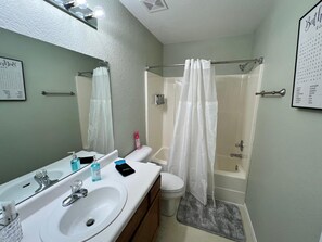 Une salle de bain avec un lavabo blanc, un miroir, des toilettes et une douche.